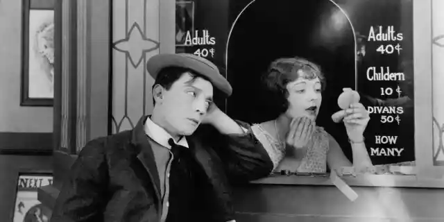 1924: American comedian Buster Keaton (1895-1966) standing outside the box office clutching his dollar bill while Ruth Holly applies her make-up in the film &#039;Sherlock Junior&#039;.
